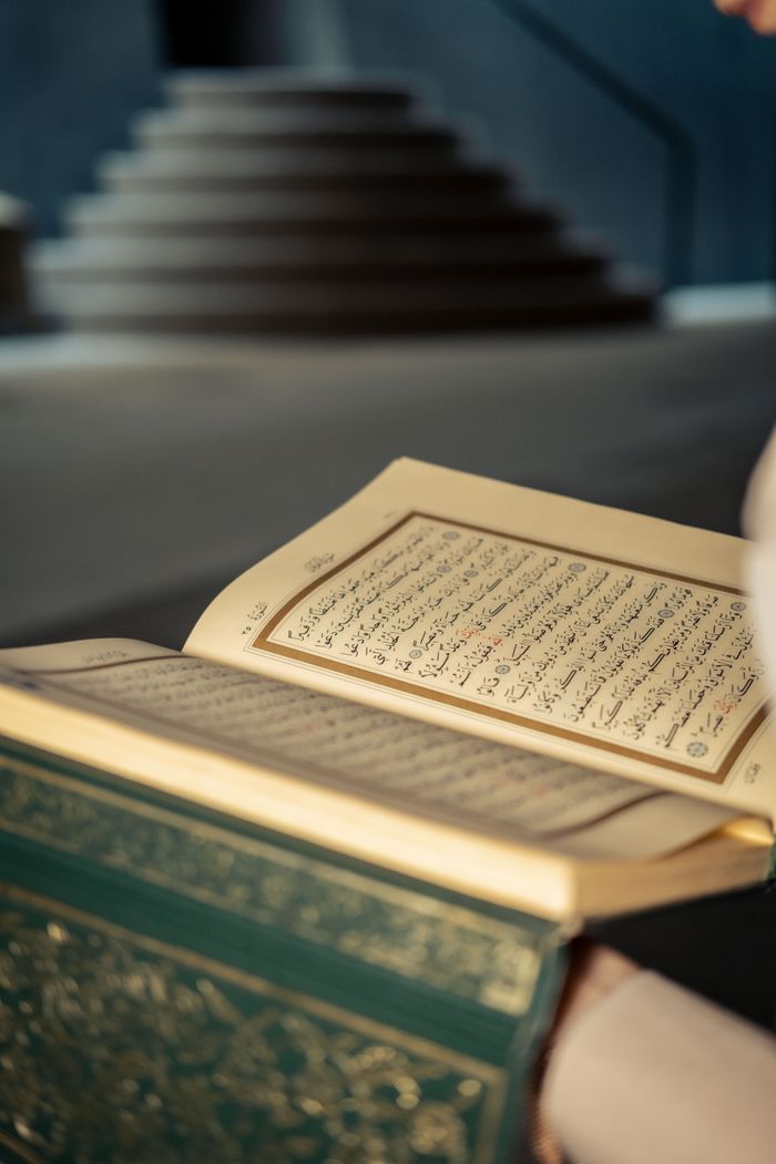 services-02 A close-up view of an open Quran with Arabic text inside a mosque setting, focused on religious literature.