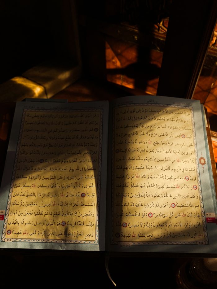 services-01 A Quran open under warm sunlight, casting serene shadows indoors.