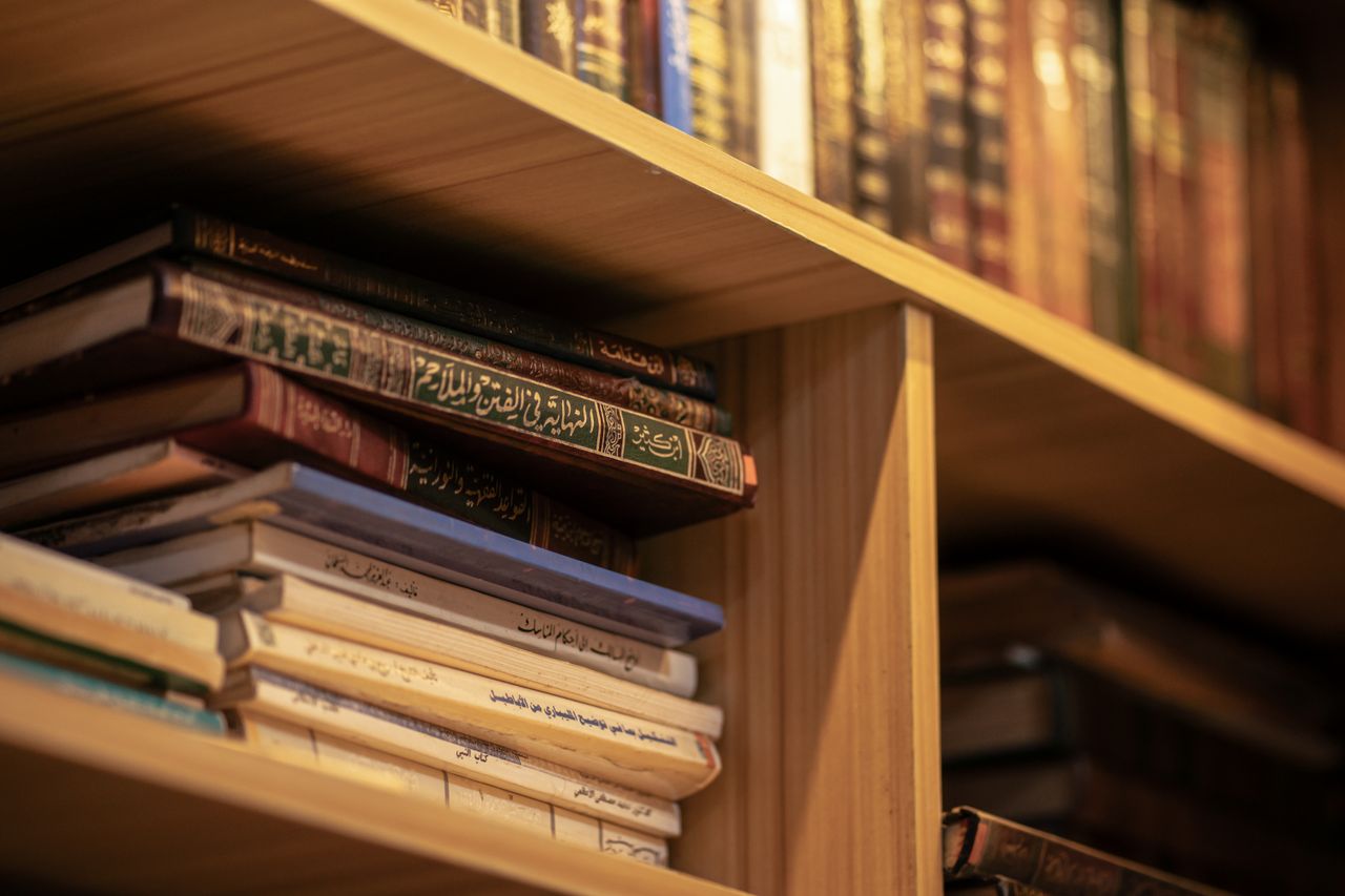 about-img A stack of Islamic religious books on a wooden shelf, highlighting Arabic scripts and cultural significance.